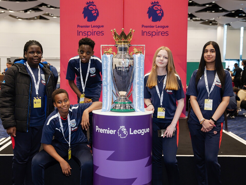 Five students standing next to the Premier League trophy, Premier League Inspires banners in the background.