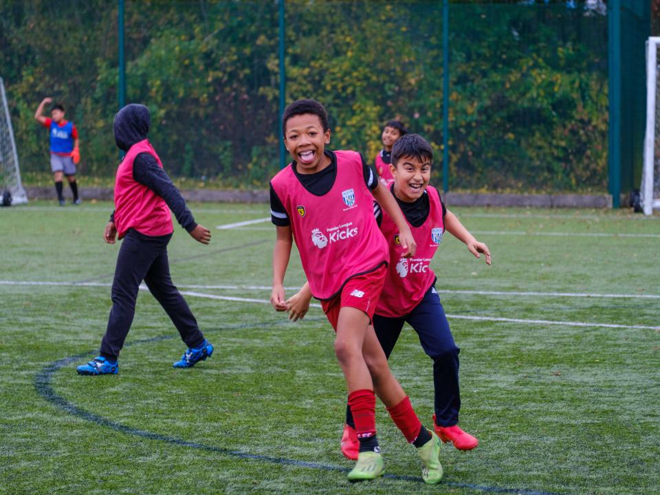 Two players celebrating in pink Premier League Kicks bibs.