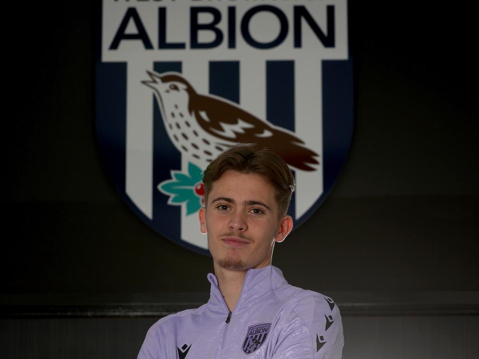 Isaac Price looking at the camera stood in front of a WBA badge 