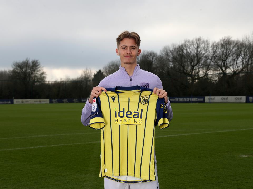 Isaac Price holding up a WBA yellow away shirt 