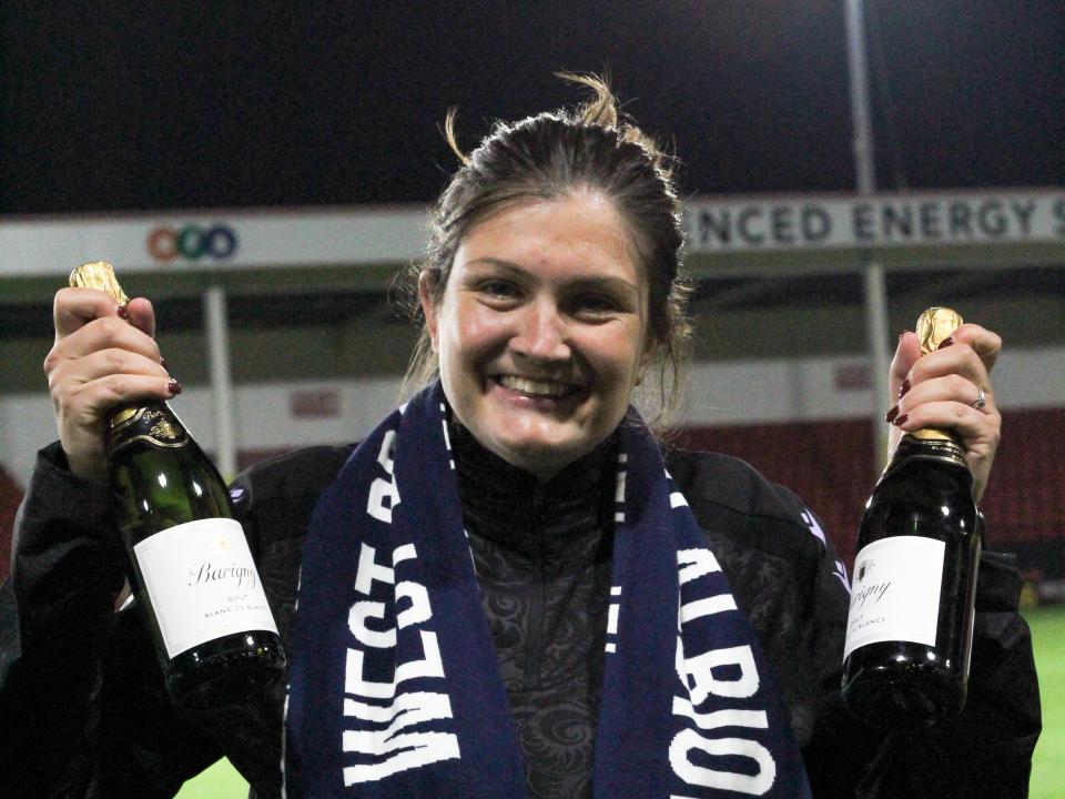 Siobhan Hodgetts-Still smiling at the camera while holding up two bottles of champagne 