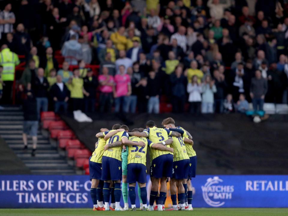 An image of the Albion players in a team huddle, with supporters behind them