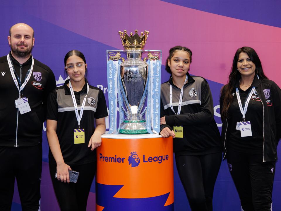 Staff and participants standing next to the Premier League trophy