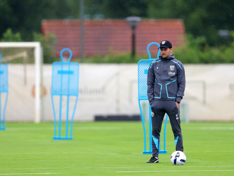 Ryan Mason watching training in the rain stood next to a mannequin in a cap