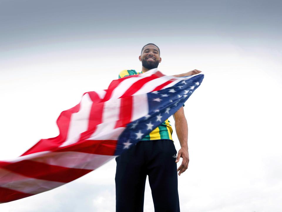 George Campbell smiling while stood in an away WBA shirt waving an American flag