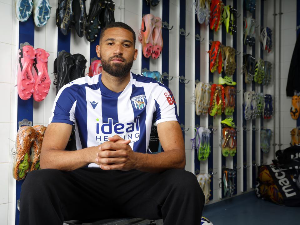 George Campbell sat in the boot room in a home WBA shirt smiling at the camera 