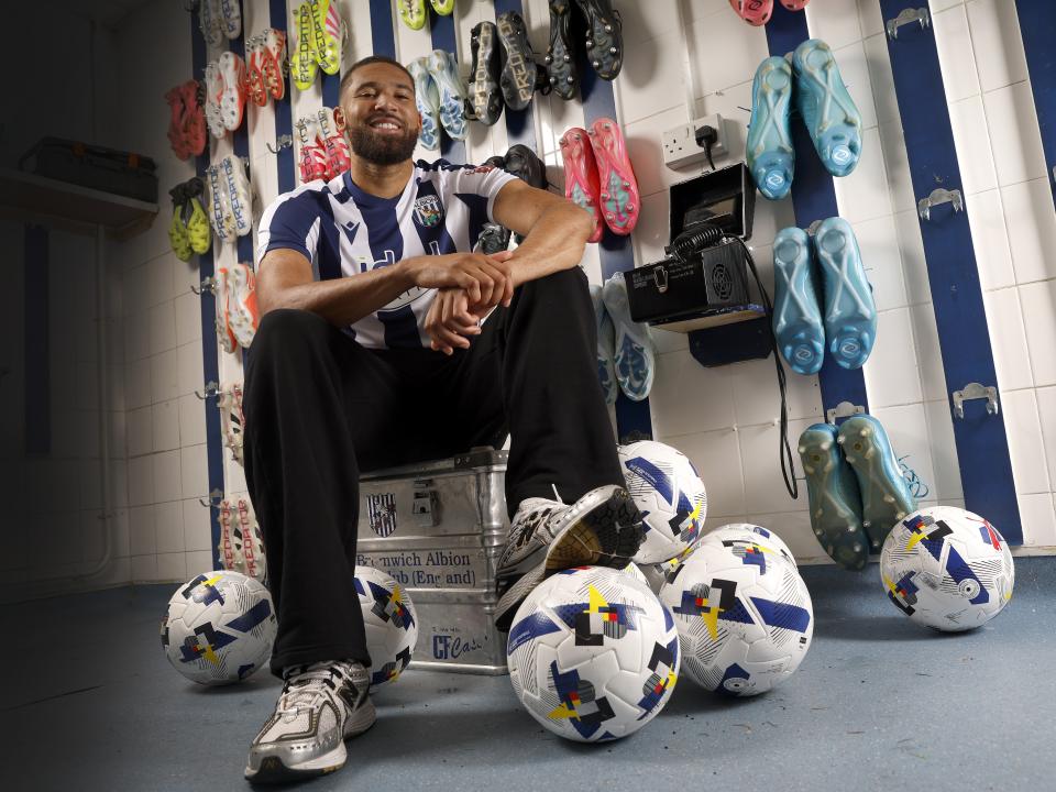 George Campbell sat in the boot room in a home WBA shirt smiling at the camera with a ball under his foot