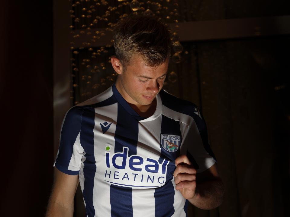 Aune Heggebø pulling the badge and looking at it while wearing a WBA shirt