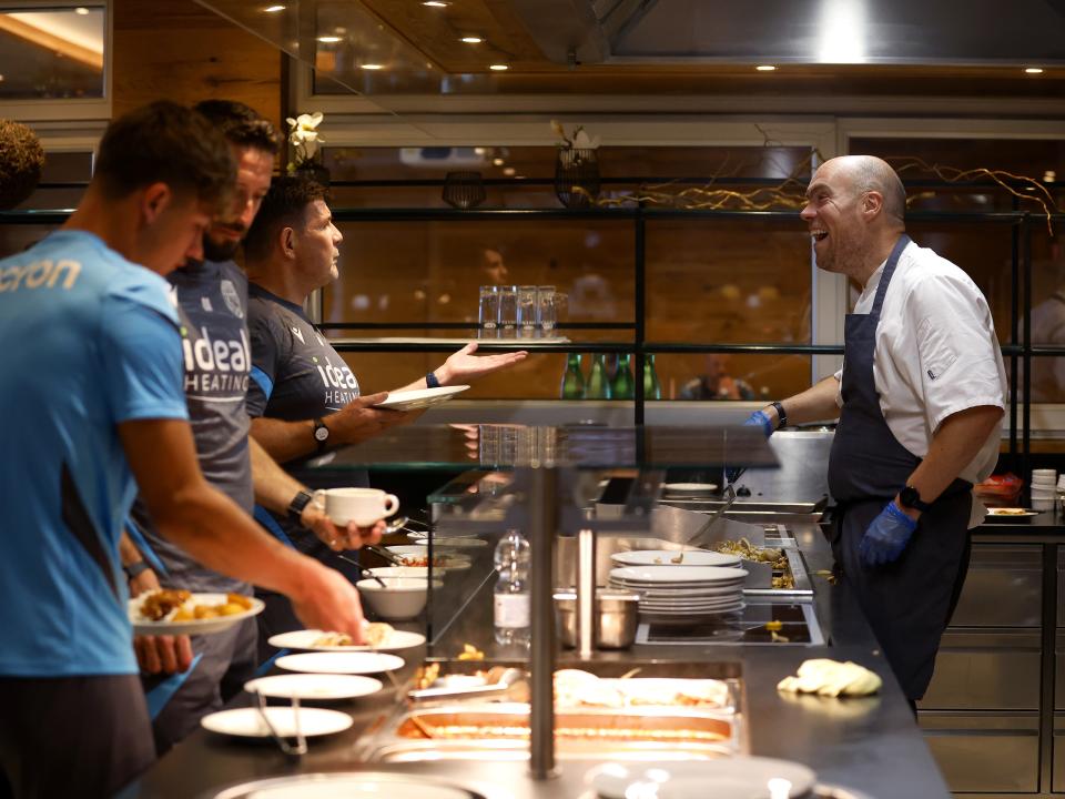 A WBA chef laughing with players and staff in the kitchen at the hotel