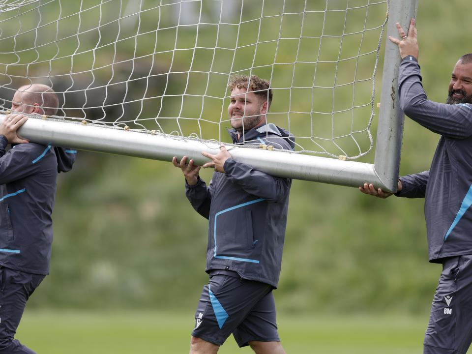 Three Albion staff members carrying a goal on a training pitch 
