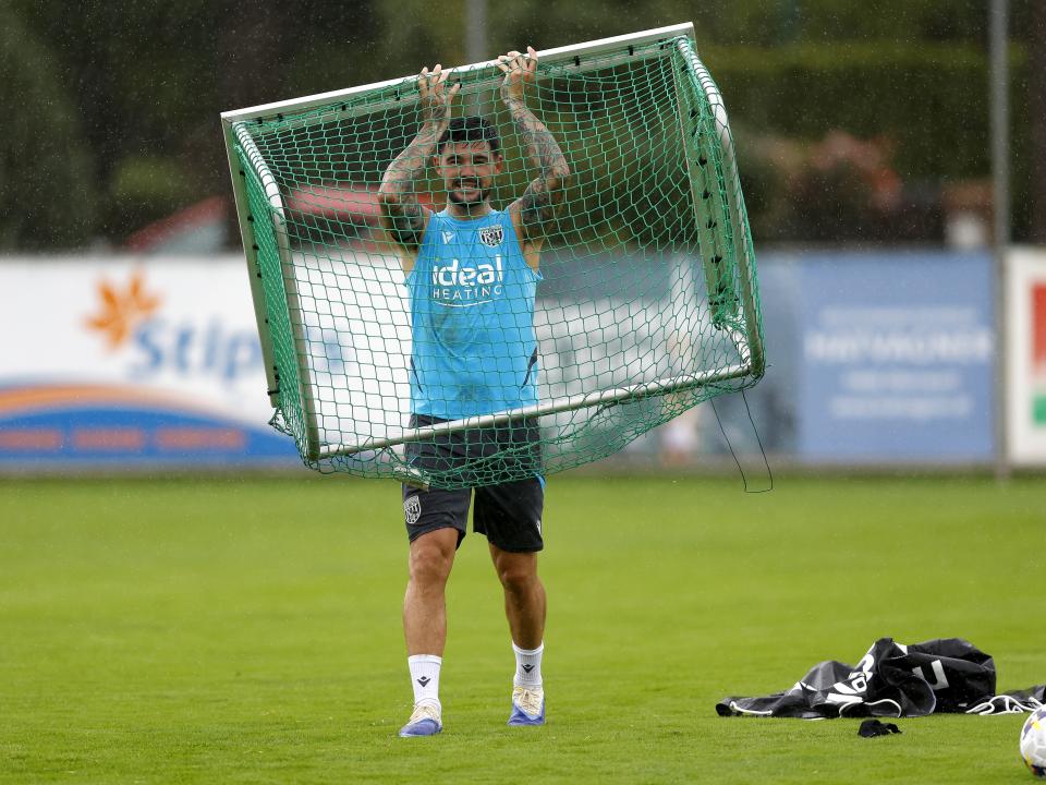 Alex Mowatt holding up a mini goal above his head during a training session in the rain