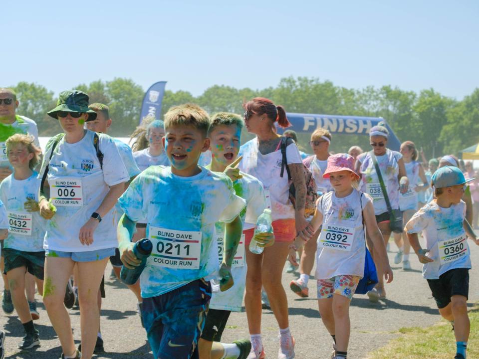 Large group of second wave runners, covered in paint, leaving the start line.