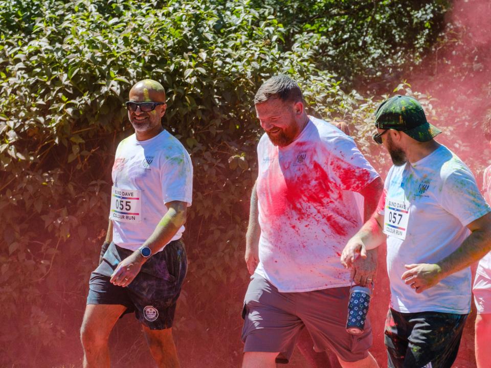 Runners passing colour station being douse with red powder.