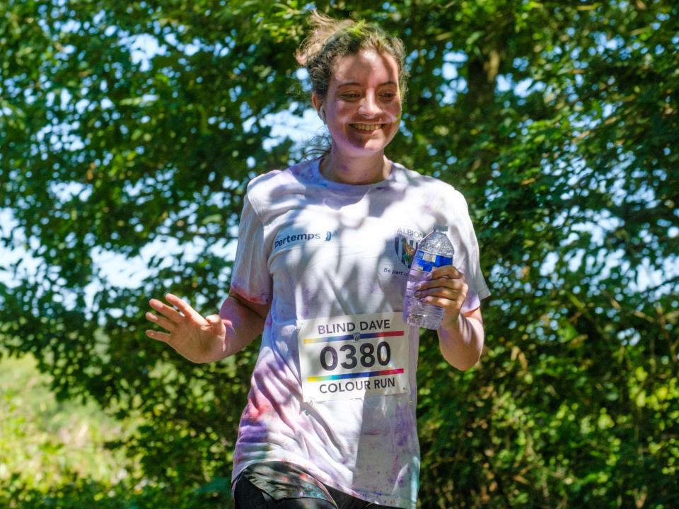 MP Sarah Coombe, waving and holding a bottle of water, as she running pass the pond.