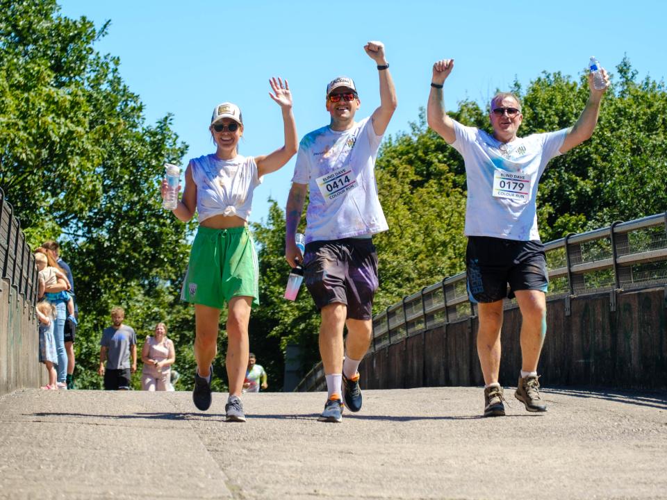 Three participants walking across the motorway bridge, with raised arms.