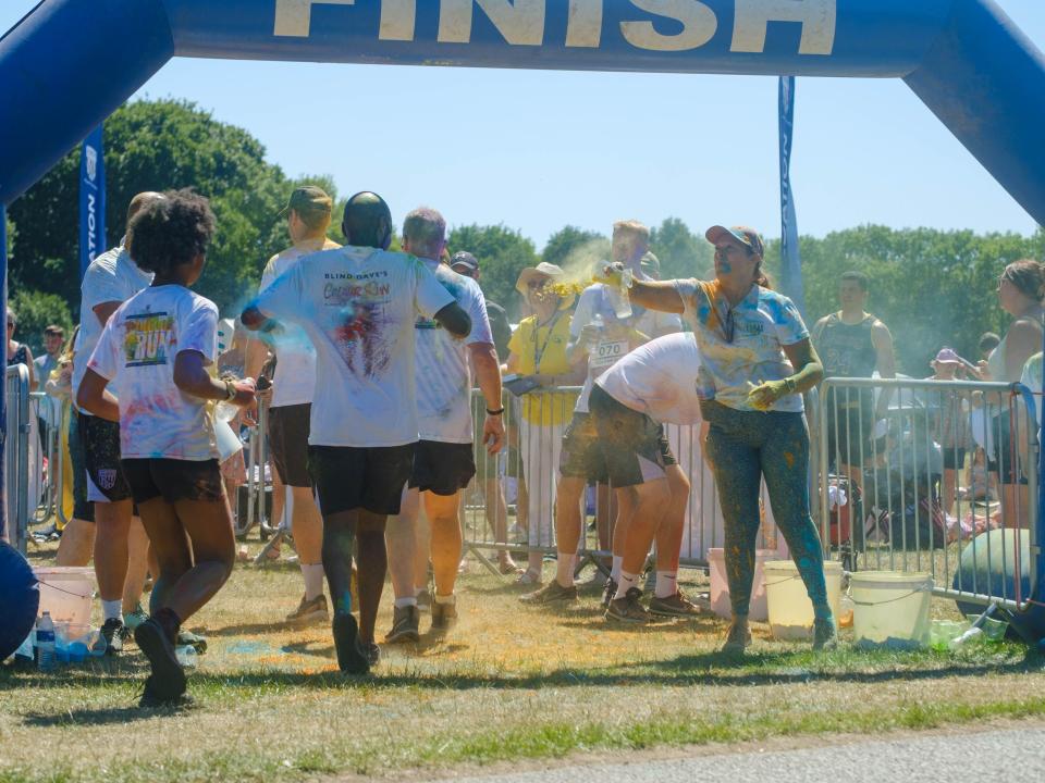 Runners crossing the finish line, as staff and volunteers throw paint.