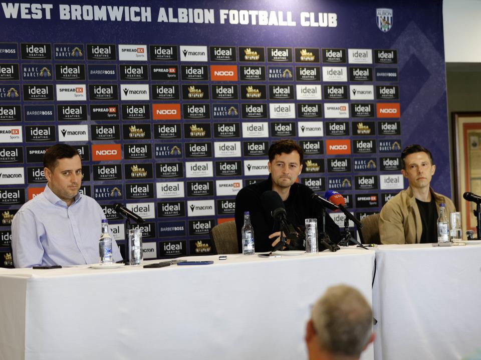 Ryan Mason and Andrew Nestor talking to members of the media in front of a press conference sponsor board and behind a number of microphones