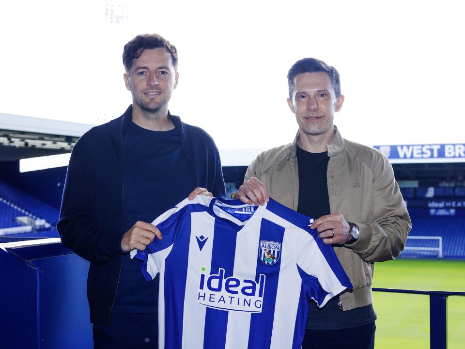 Ryan Mason and Andrew Nestor smiling at the camera while holding up a home WBA shirt in front of the West Stand at The Hawthorns