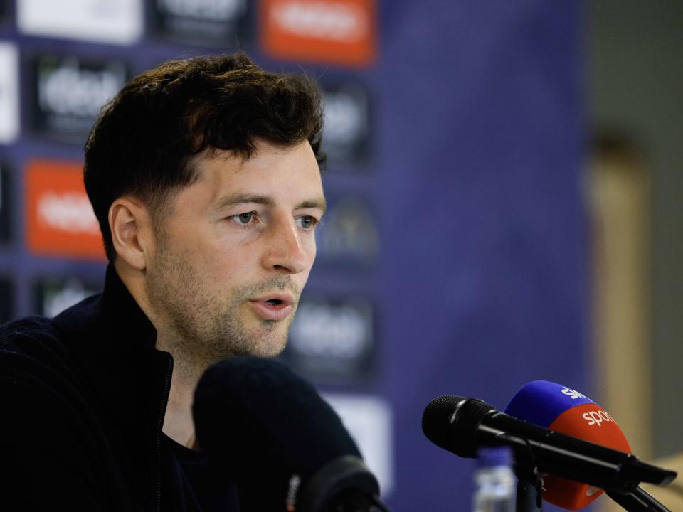 Ryan Mason talking to members of the media in front of a press conference sponsor board and behind a number of microphones