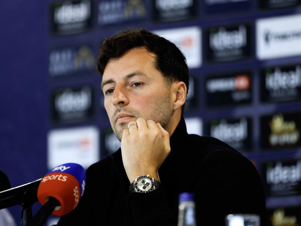 Ryan Mason talking to members of the media in front of a press conference sponsor board and behind a number of microphones