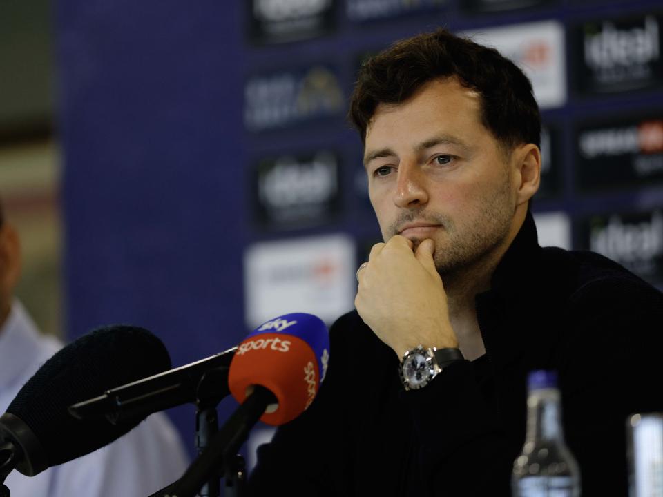 Ryan Mason talking to members of the media in front of a press conference sponsor board and behind a number of microphones