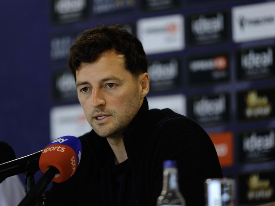 Ryan Mason talking to members of the media in front of a press conference sponsor board and behind a number of microphones