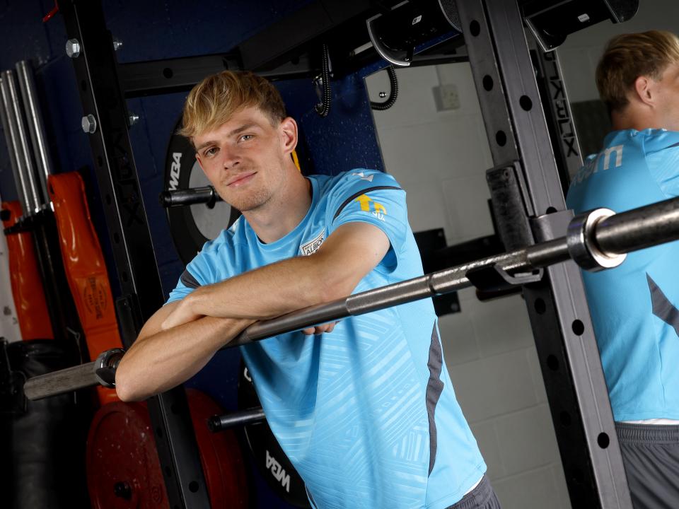 Toby Collyer smiling at the camera while leaning on a bar in the gym