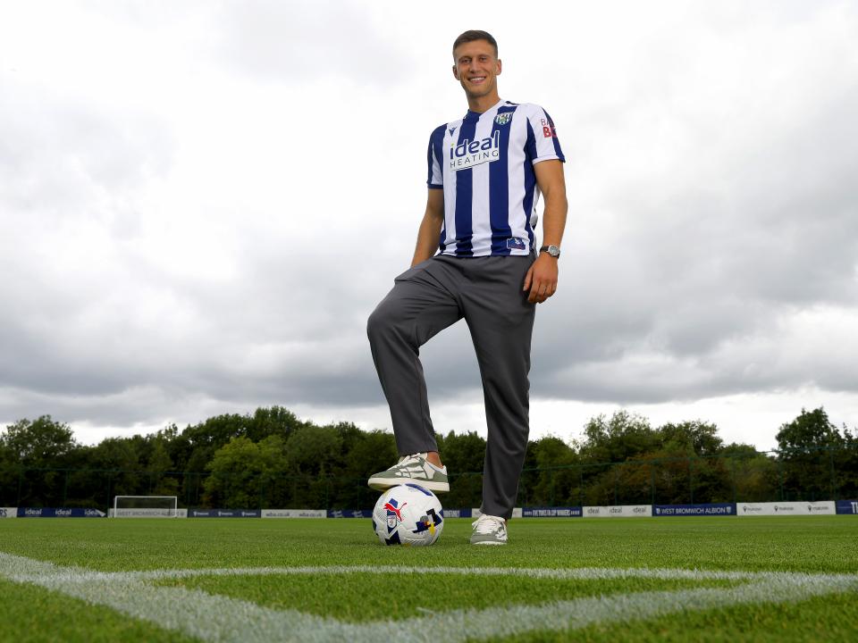 Krystian Bielik smiling at the camera while stood in the home shirt with one foot on the ball