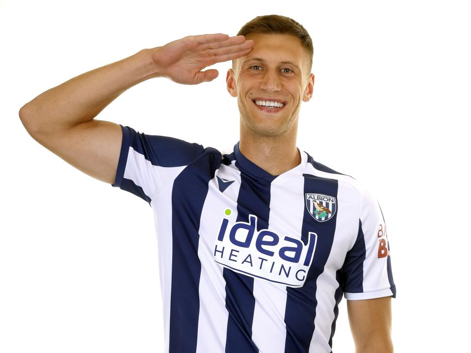 Krystian Bielik in the home kit smiling at the camera with his hand to his head