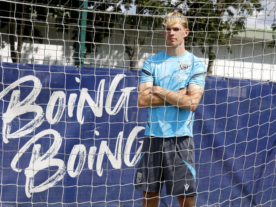 Toby Collyer looking through a goal net with his arms crossed next to branding saying "boing boing'