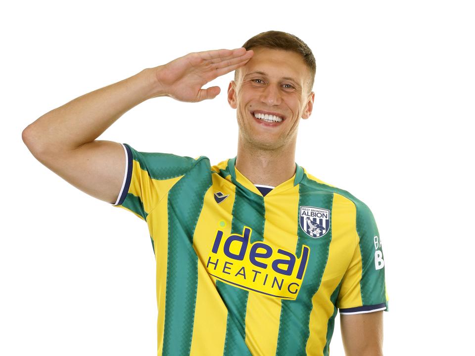 Krystian Bielik in the green and yellow away kit smiling at the camera with his hand to his head