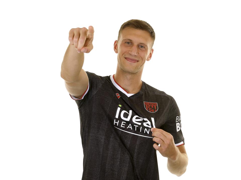 Krystian Bielik in the black away kit smiling and pointing at the camera