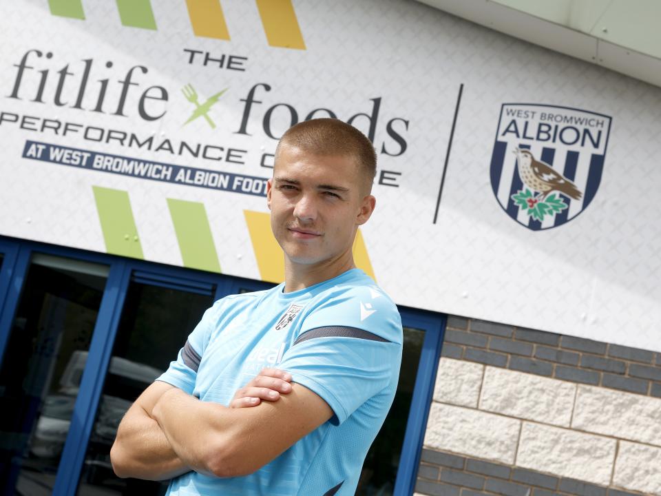 Alfie Gilchrist outside the front of the training ground with his arms folded looking at the camera 