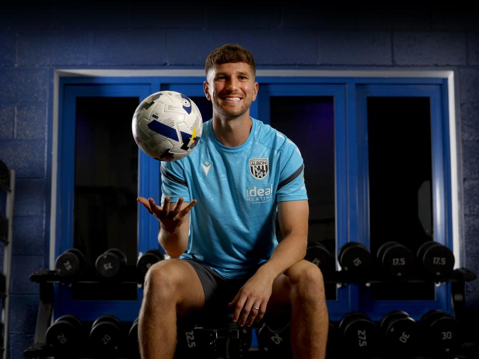 Chris Mepham smiling at the camera while holding a ball and being sat down in the gym