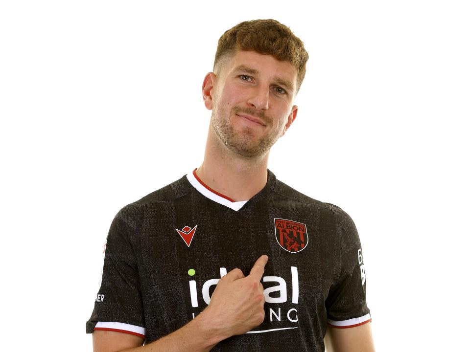 Chris Mepham in the black away kit smiling at the camera and pointing to the badge 