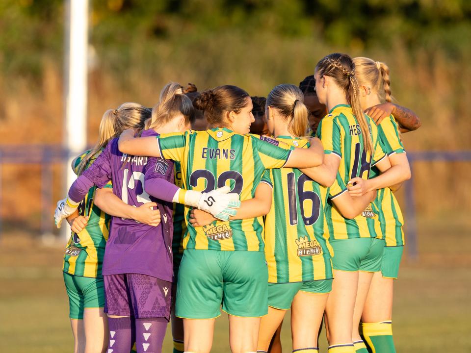 An image of Albion Women in a team huddle wearing yellow and green