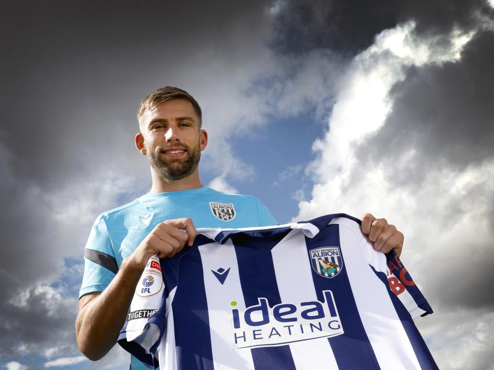 Charlie Taylor smiling at the camera while holding up a home WBA shirt