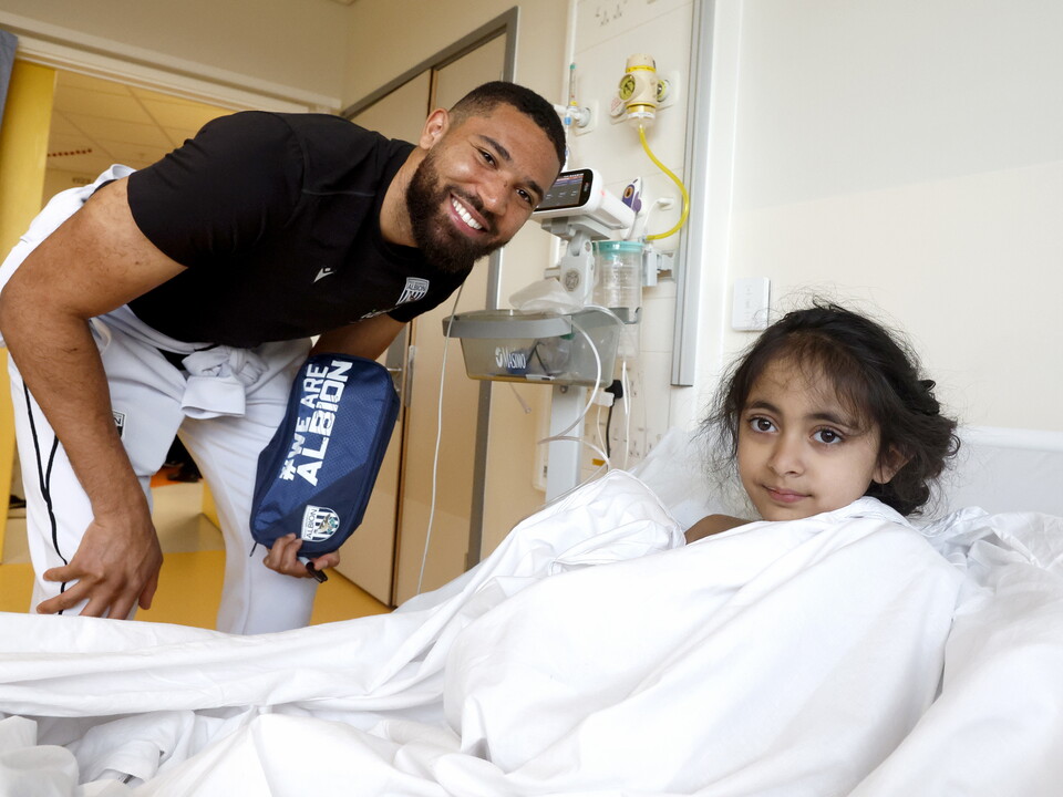 George Campbell posing for a photo with a poorly child in a bed on a ward at the Midlands Met hospital