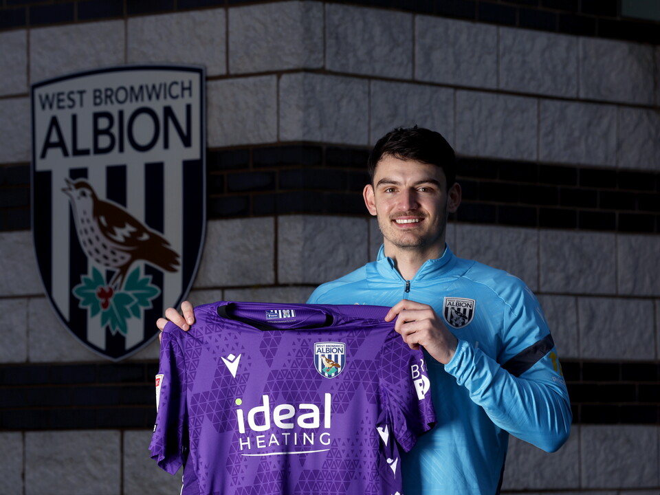 Max O'Leary smiling at the camera while holding up a WBA shirt 