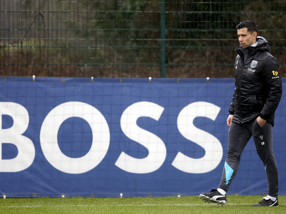 Eric Ramsay watching training in the rain while stood next to a sign that says 'BOSS'