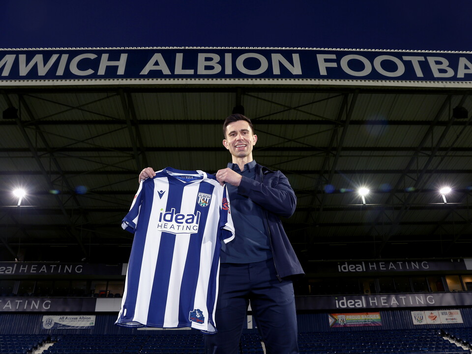 Eric Ramsay smiling at the camera and holding up a home WBA shirt at The Hawthorns