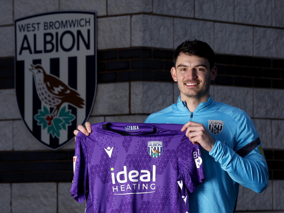 Max O'Leary smiling at the camera while holding up a home WBA GK shirt 