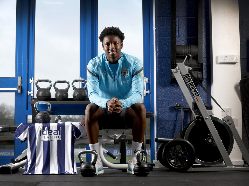 Jamaldeen Jimoh-Aloba smiling at the camera while sat on a bench in the gym with a home WBA shirt next to him