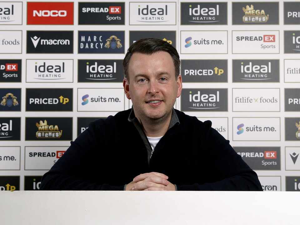 Dominic Price smiling at the camera in front of sponsor boards