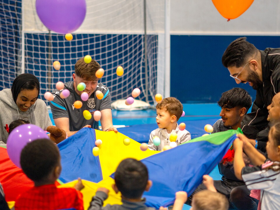 Staff, parents & participants doing a parachute activities with easter eggs and balloons.