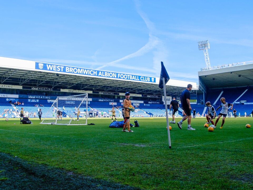 Players warming up on the pitch with the West Stand in the background.