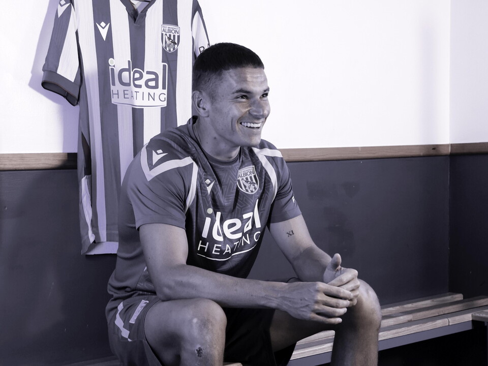 Conor Townsend smiling while sat down in a dressing room with the home shirt hanging over his head 