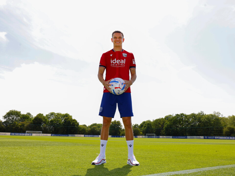 Conor Townsend smiling at the camera while stood in the away kit out on a training pitch and holding a ball
