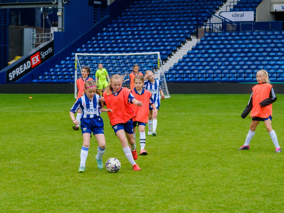 Two girls battling for the ball at The Hawthorns, with teammates in the background.