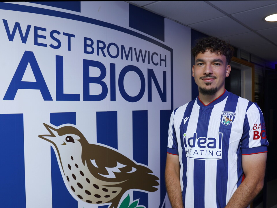 Nolan Galves in the home shirt smiling at the camera while stood in front of a big WBA badge 